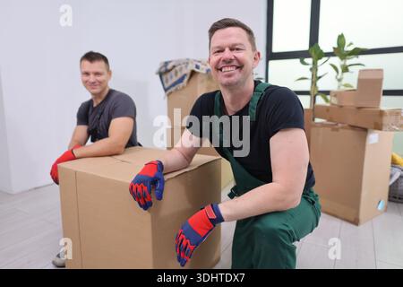 Two cheerful movers organizing boxes in a bright, modern living space during a lively relocation process Stock Photo