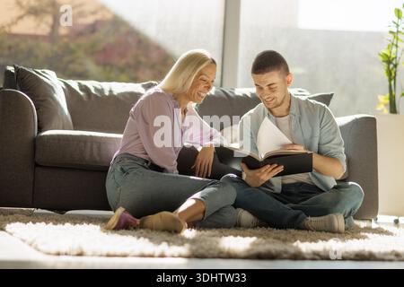 Happy couple sitting on the floor and looking at a book in the living room Stock Photo