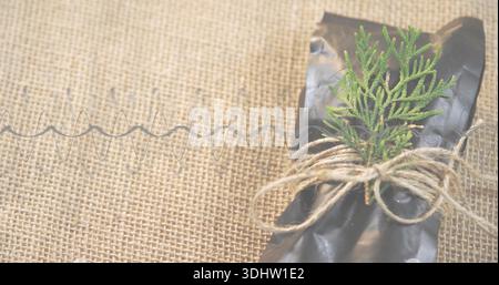 Displaying black wrapped parcel with jute twine, green sprig and metal coil on burlap, copy space Stock Photo