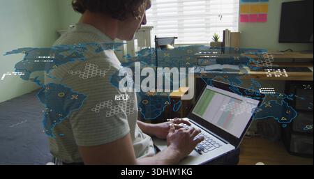 Working man in striped tee, dark shorts, typing charts on laptop in bedroom, with world-map overlay Stock Photo