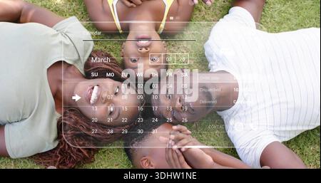 Lying family smiling wearing green top and yellow tank on grassy lawn, March calendar overlay Stock Photo