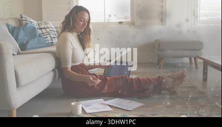 Reading woman in rust pants, light top, sitting on rug at home with laptop, documents, mug Stock Photo