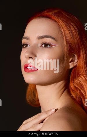 Bright red haired woman showcases contemporary makeup against a dark, artistic background. Stock Photo