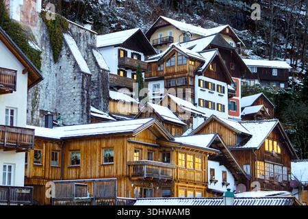 Traditional wooden Alpine chalets with snow-covered roofs clustered on a steep hillside in a European mountain village during winter season. Stock Photo