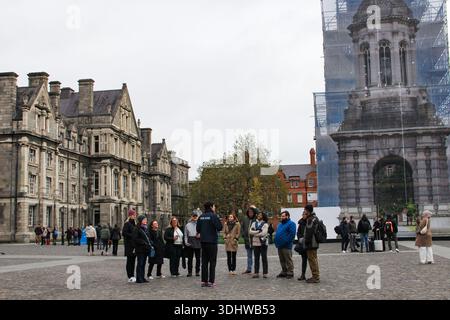 A diverse group of tourists on a guided walking tour in a historic university courtyard with Gothic architecture and scaffolding tower. Stock Photo