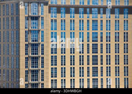 Close-up view of a tan stone corporate building facade with a grid of blue reflective windows and classical architectural details in daylight. Stock Photo