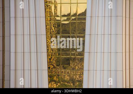 Architectural detail of a modern building featuring a central strip of reflective gold glass panels set between white vertical ribbed pillars. Stock Photo