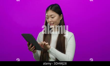 Woman smiling using tablet against vibrant pink background showcasing cheerful interaction with technology Stock Photo