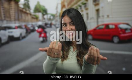 Woman beckons with hands on street in green longsleeve top near parked car; invitation welcome connection. Stock Photo