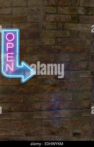 Ronda, malaga, spain Glowing pink and blue neon sign displaying open and an arrow pointing right, fixed to an old brick wall Stock Photo