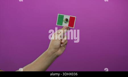 Man hand holding mexican flag embroidery against a vibrant pink wall, showcasing national pride and craft on an isolated colored background with empha Stock Photo