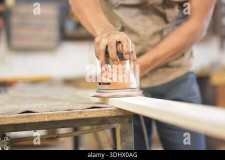 Carpenter sanding wood on a workbench. Close-up of a man using a hand sander Stock Photo