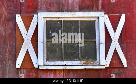 Rustic, framed, red barn window has cracked glass and covered in grime.  It is trimmed in white. Stock Photo