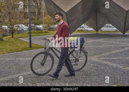 Man pushing bicycle, walking a bike, at Skulpturengarten Tucherpark Zwillingsplastik in city Munich, Bavaria, Germany, commute, casual, commuter, way Stock Photo