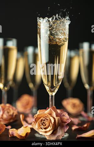 Sparkling wine made of glass surrounded by other glasses and rose petals on a black background Stock Photo