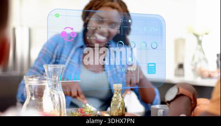 Reviewing woman with braids in blue top analyzing hologram charts at kitchen table, with watch Stock Photo