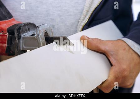 Carpenter holds hand saw while cutting piece of material in equipment setting is well lit Stock Photo