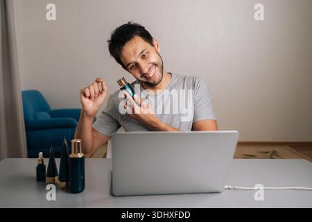 Positive bearded male vlogger creating skincare content online, reviewing beauty serum and making heart gesture with hands, connecting with audience Stock Photo