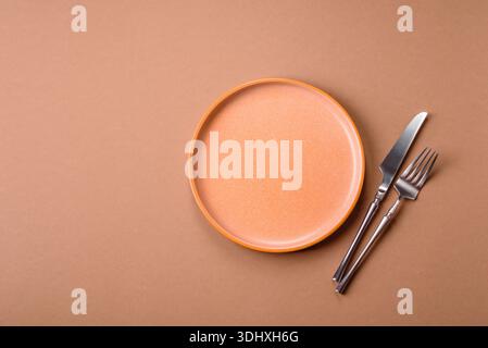 An empty round ceramic plate, knife, and fork as a dining table setting. An empty plate as a backdrop for your design Stock Photo