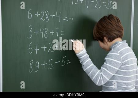 Schoolboy doing math on chalkboard in classroom Stock Photo