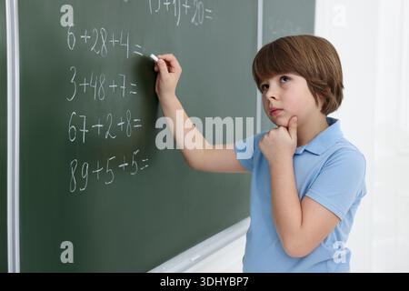 Schoolboy doing math on chalkboard in classroom Stock Photo