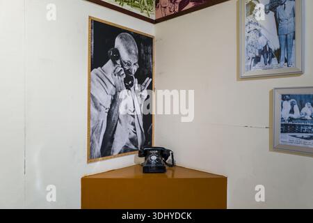 Delhi, India - March 29, 2024: A vintage black telephone is displayed beneath a large black-and-white photograph of Mahatma Gandhi using a telephone, with additional framed historical photographs on the wall at the National Gandhi Museum. Stock Photo