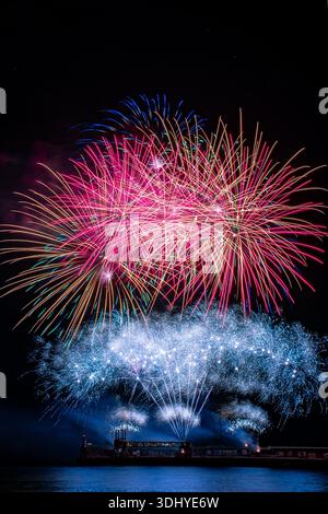 a spectacular fireworks display exploding in vibrant colors against a deep black night sky. Bursts of red, pink, blue, and gold light radiate outward Stock Photo