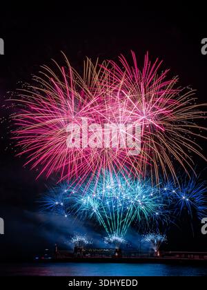 a spectacular fireworks display exploding in vibrant colors against a deep black night sky. Bursts of red, pink, blue, and gold light radiate outward Stock Photo