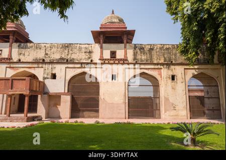 Fatehpur Sikri, India - March 12, 2024: The image shows the exterior wall of the Hamman garden at Jodha Bai Palace with three large arched gates covered by metal grilles, two domed pavilions above, a small balcony, and a manicured lawn with flower beds in the foreground. Stock Photo