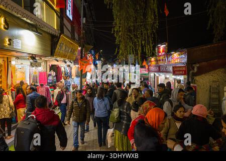Darjeeling, India - March 26, 2024: A busy street in Darjeeling is filled with people shopping at night, with illuminated storefronts displaying clothing and signage for pashmina shawls and cashmere goods. Stock Photo