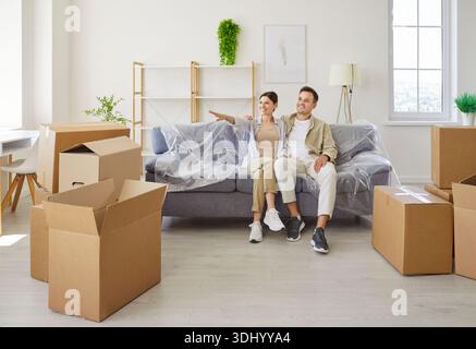 Smiling couple planning new apartment layout while sitting on sofa amid boxes Stock Photo