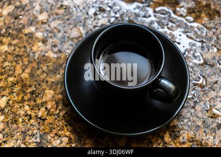 Top-down view of a black coffee cup on a speckled granite with water drops. This minimalist and modern image evokes the feeling of a morning routine, Stock Photo