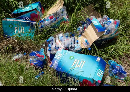 Discarded cardboard cartons and empty plastic water bottles are scattered in grass, forming a pile of litter in an outdoor area in Fiji. Stock Photo