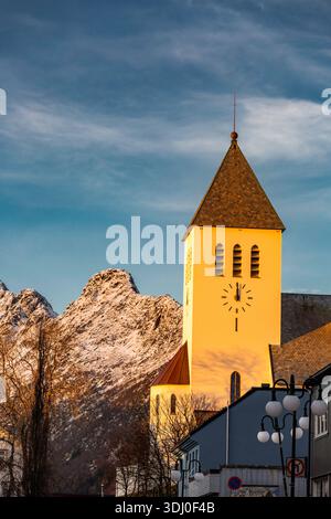 Svolvear, Lofoten Island, Norway Clock tower with a clock face on the side of it. The clock is set at 10:30. The sky is blue and the sun is setting. T Stock Photo