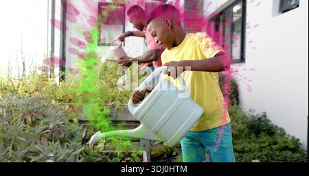 Leaning child in yellow tee tipping white watering can into raised beds on terrace, magenta overlay Stock Photo