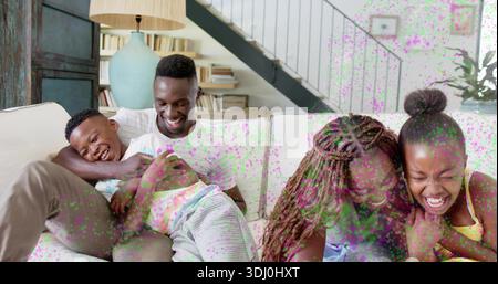 Laughing family sitting on light couch in living room showing white tee yellow tank turquoise lamp Stock Photo