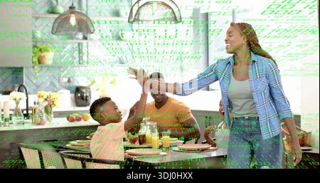 Leaning mother in blue plaid shirt giving high-five to boy in modern kitchen, with code overlay Stock Photo