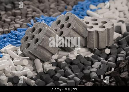 A close-up view from above, three large gray cylindrical catalysts resting on a dense mixture of gray,white, and blue multi-colored industrial pellets Stock Photo