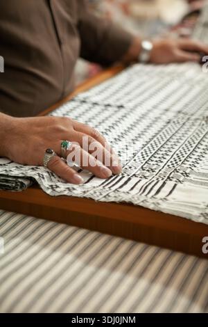 A close-up of a person's hands resting on a black and white patterned cloth on a table, highlighting the fabric's precise geometric design. Stock Photo