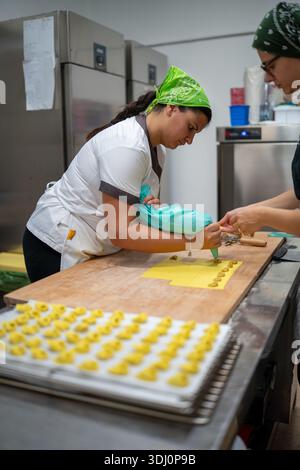 Two women in a kitchen meticulously crafting tortelli, a classic Italian stuffed pasta, using a piping bag and fresh dough Stock Photo