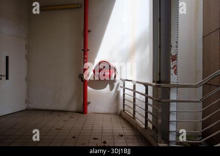 A fire hose reel on the wall in a stairway highlighted by a shaft of sunlight located at a overpass entrance in Singapore Stock Photo