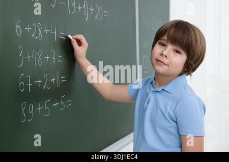 Schoolboy doing math on chalkboard in classroom Stock Photo
