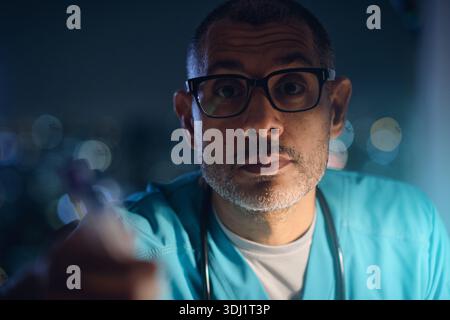 Male doctor in scrubs and glasses looking directly at viewer during the night Stock Photo