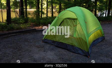 Tent designed for backpacking lit from inside as the sun rises over a lake behind seen through the trees. Stock Photo