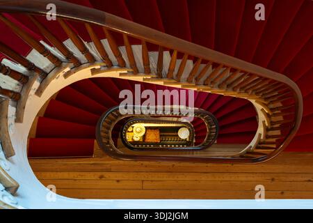 Colorful spiral staircase interior with red walls, wooden steps, and curved railings viewed from above. Stock Photo