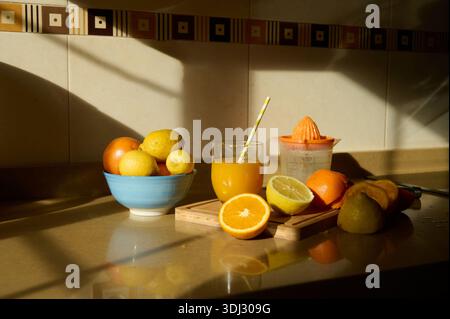 A colorful still life of oranges, lemons, limes, and a glass of orange juice on a wooden board, bathed in warm sunlight. Stock Photo