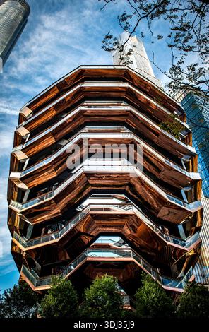 The Vessel at Hudson Yards in Manhattan, New York City, rising against a blue sky and surrounded by Midtown skyscrapers. Stock Photo