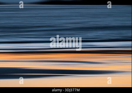 A serene seascape at sunset features horizontal streaks of warm orange, deep blue, and soft gray, creating a painterly, abstract effect. The blurred m Stock Photo