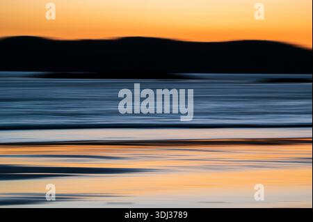 A serene seascape at sunset features horizontal streaks of warm orange, deep blue, and soft gray, creating a painterly, abstract effect. The blurred m Stock Photo