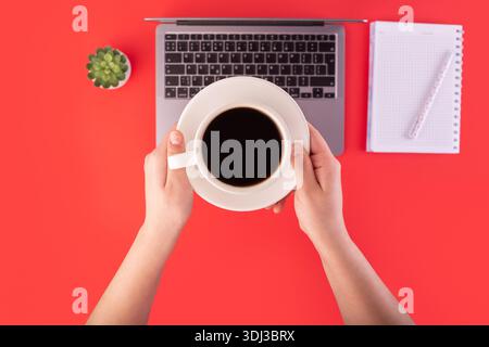 Top view photo of notebook, grey laptop with holding hands cup of black coffee on isolated red background. coffee break concept Stock Photo